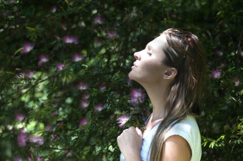 Woman taking a deep breath outside by greenery